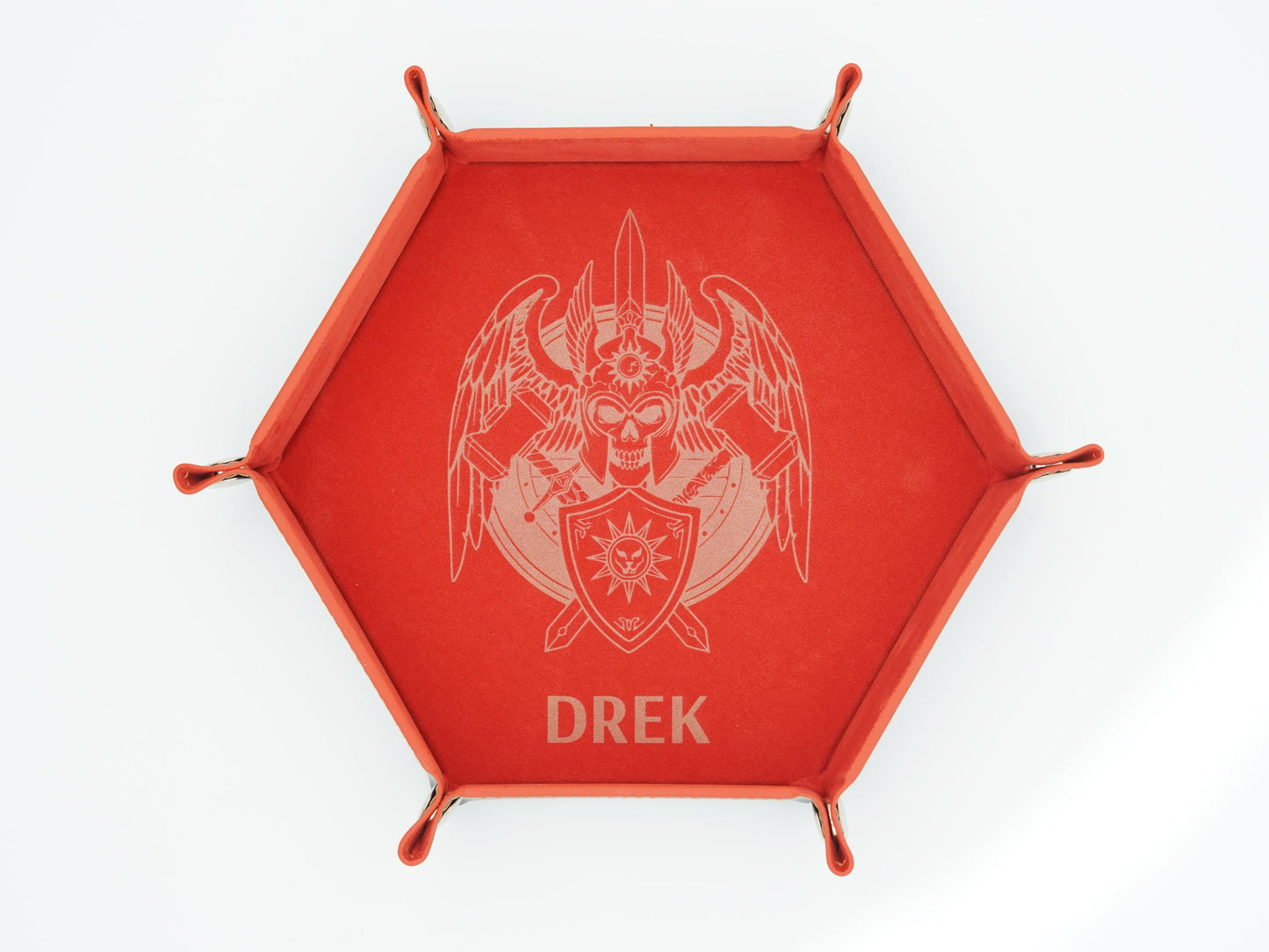A red hexagonal tray with four small feet and a raised rim, featuring a light engraved emblem of a winged skull with crossed weapons and the name 'DREK' below, shown on a white background.