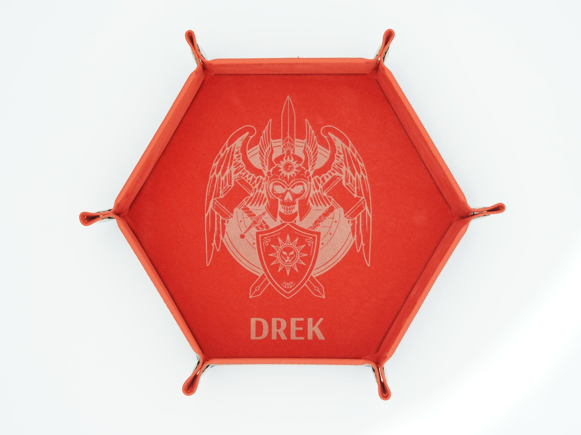 A red hexagonal tray with four small feet and a raised rim, featuring a light engraved emblem of a winged skull with crossed weapons and the name 'DREK' below, shown on a white background.