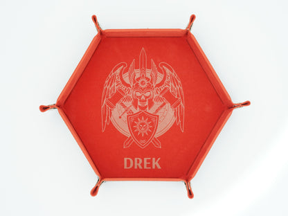 A red hexagonal tray with four small feet and a raised rim, featuring a light engraved emblem of a winged skull with crossed weapons and the name 'DREK' below, shown on a white background.