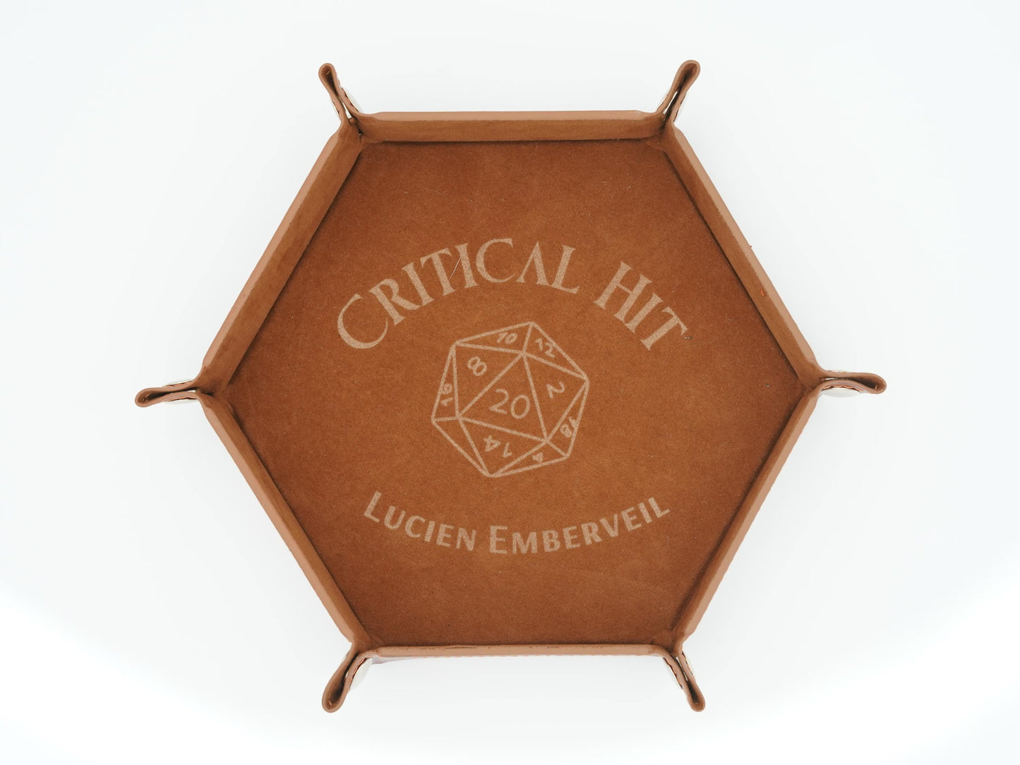 A hexagonal brown leather tray with metal corner supports, featuring an engraved design on the top that reads 'CRITICAL HIT' above a 20-sided die icon and 'LUCIEN EMBERVEIL' below, shown on a white background.